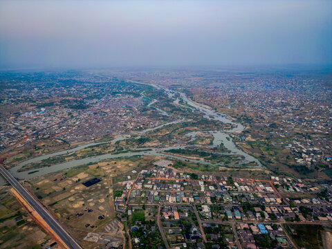Aerial view of the winding Kaduna River cutting through the city's landscape, a tapestry of buildings and vegetation under a hazy sky, Kaduna, Kaduna, Nigeria.