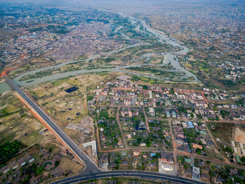 Aerial view of the Kaduna River snaking through the city, reflecting the sky's soft light between dense buildings and lush greenery, Kaduna, Kaduna, Nigeria.