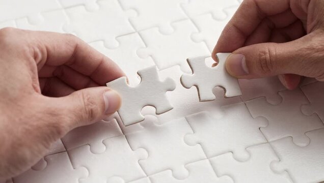 two hands placing two pieces jigsaw puzzle together white surface puzzle pieces arranged way suggests part