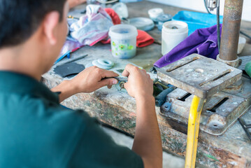 Man carefully working on a piece of jade at his workshop table, using hand tools in a traditional jewelry-making process. © Kenneth Arrieta 