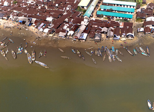 Aerial view of boats dotting the waterfront next to buildings with rusty rooftops, creating a vibrant contrast against the muddy waters, Khana, Bori, Nigeria.