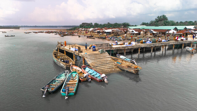 Aerial view of the bustling Kaa Waterfront, where boats bob gently in the river, reflecting the sky's soft light, contrasting with the vibrant life on the pier, Khana, Bori, Nigeria.