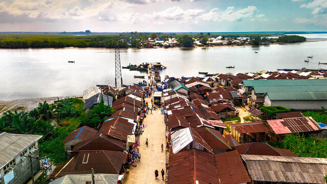 Aerial view of a bustling waterfront with buildings with rusty roofs and boats dotting the calm river, Kaa Waterfront, Khana, Bori, Nigeria.
