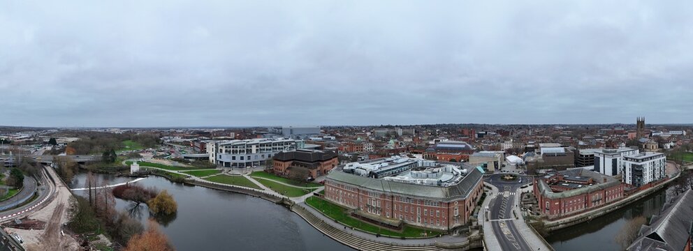 Aerial view of the serene River Derwent winding through Derby, contrasting with the red brick buildings and modern architecture under a vast, cloudy sky, Derby, England, United Kingdom.