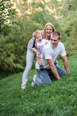 Happy family is playing cheerfully in the park in the summer. Father holding kid on shoulders.