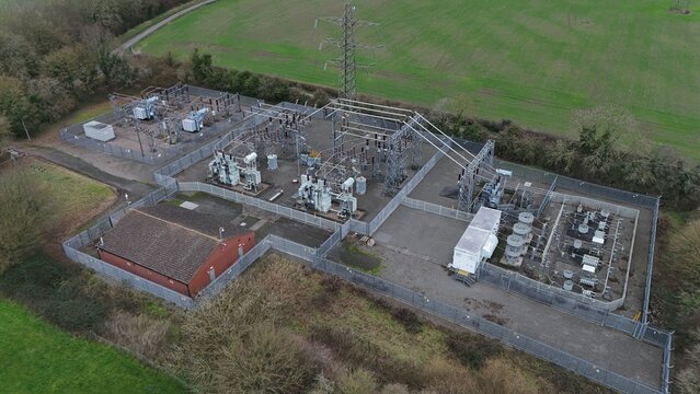 Aerial view of an electrical substation with transformers and power lines standing stark against the verdant landscape, Melton Mowbray, England, United Kingdom.