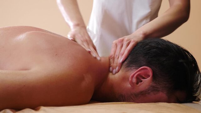 Handsome man enjoying neck massage in spa center. Relaxed male client lying on bed in beauty parlor as masseur rubbing skin. therapist making client athlete neck massage in spa salon. Professional
