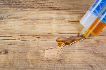 Double syringe with epoxy gel glue spilling on genuine brown leather texture, soft focus close up
