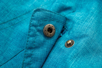 Close-up of a blue-green linen blend waterproof jacket pocket cover with metallic snap fasteners