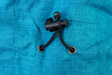Black plastic cord lock mechanism on a piece of bright blue fabric, which is a common component of outdoor or athletic apparel, soft focus close up