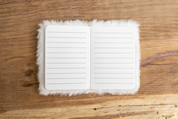 White furry cover on an empty opened notebook with lined pages on wooden desk background, abstract minimal backdrop