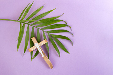 Palm tree leaf and wooden crucifix on purple background with copy space