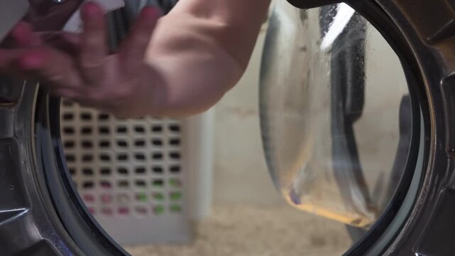 Finding a Lost Sock in the Washing Machine. A close-up of a man's hand as he gropes around in a washing machine, searching for forgotten items. A heart-print sock is retrieved