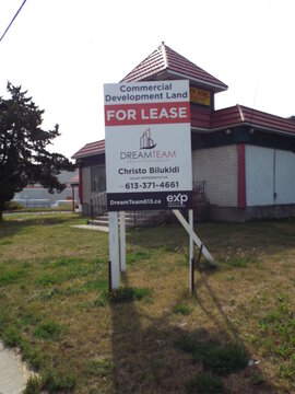 Gloucester, ON, Canada-July 5,2025: A "Commercial Development Land FOR LEASE" sign by "DreamTeam Real Estate Group" stands in front of a vacant red-roofed building on Cyrville Road.