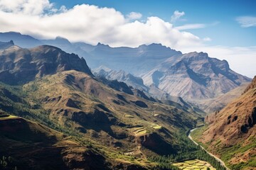 Winding road traversing through a dramatic mountain valley featuring terraced farmlands under clouds