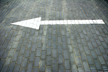 White arrow on gray brick pavement pointing forward at a public location during daylight hours