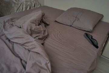 Unmade mauve bed with sleep mask on pillow in modern cozy bedroom setting.