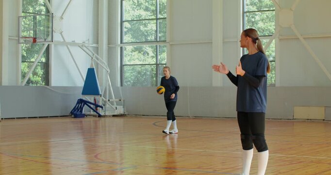 A volleyball player serves the ball, a girl from her team actively supports her and claps her hands.