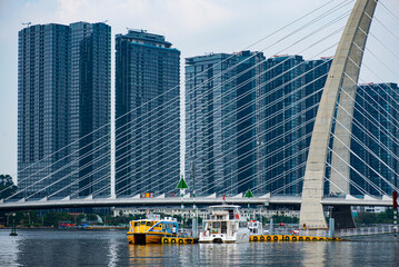 Yellow boat is on the water near a bridge. The bridge is over a river and there are many tall buildings in the background