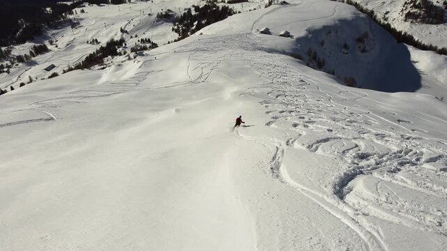 Aerial drone footage of ski touring and freeride skier descending snowy alpine mountain in winter