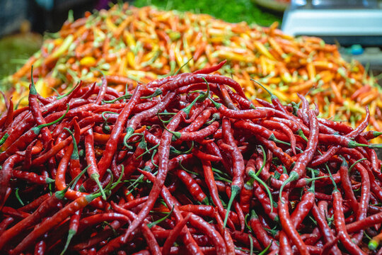 Pile of fresh red chili peppers at traditional market stall with colorful vegetable background showing spicy ingredient commonly used in Indonesian cuisine
