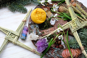 Wiccan altar for Imbolc sabbat. witchcraft, pagan magic ritual. Brigid's cross, crystals, wheel of the year, snowdrops, moon amulet on wooden table close up. symbol of Imbolc holiday, spring equinox.