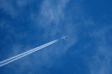 Passenger plane in flight against blue sky and clouds. Commercial airplane flying in the clear blue sky with white clouds and vapor trail.