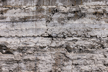 Fototapeta premium Weathered concrete wall features embedded stones and visible cracks. Outdoor setting during daytime highlights the rough texture and aged appearance of the wall.