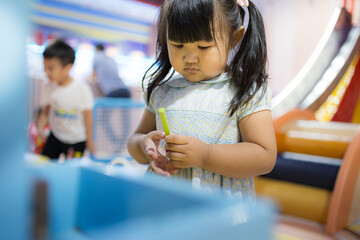 Adorable Asian Toddler Girl Playing at Indoor Playground,A cute little Asian girl with pigtails wearing a blue floral dress, focusing intently while playing with colorful toys at a modern,