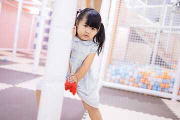 Little Asian girl playing on a red swing at an indoor playground,A cute young Asian girl with...