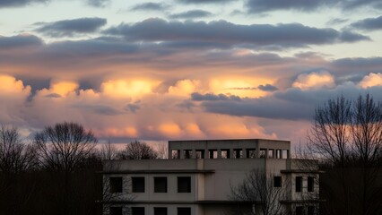 Flat roof building silhouette against dramatic sunset sky with orange and gray clouds