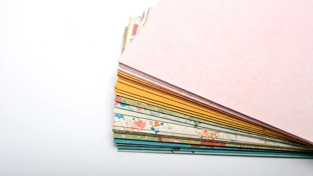 A stack of colorful papers with various designs and textures, fanning out from a white surface