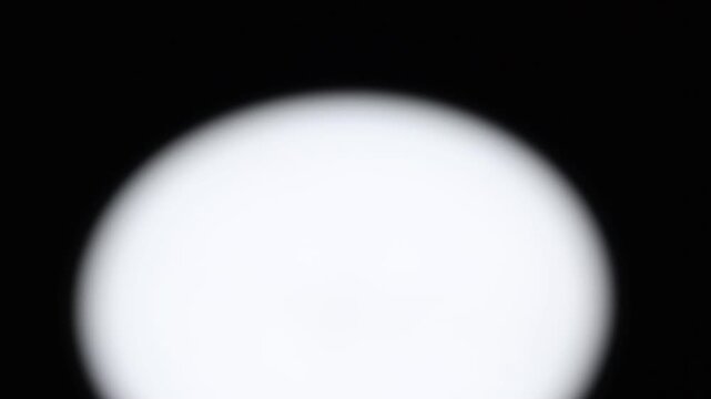 Primer plano de una luz de una lampara con un bombillo de color blanco en movimiento en la oscuridad. C&aacute;mara en movimiento