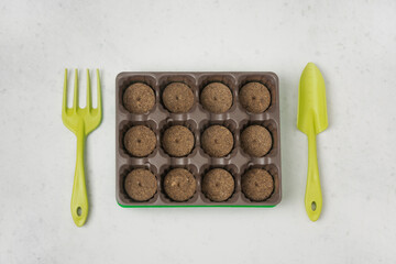 A small greenhouse with peat pellets for planting seeds and gardening tools on a gray background. Flat lay.