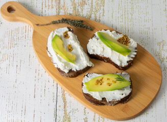 Vegetarian ricotta and avocado sandwiches with grainy mustard on a cutting board. Healthy snack