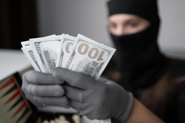 Close-up of female burglar face in balaclava stealing money and dollar cash. Masked woman thief committing criminal robbery and house burglary. Theft concept