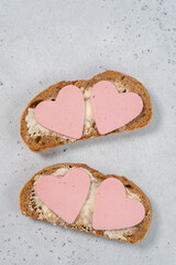 Two slices of bread with heart-shaped meat on top on a light surface seen from above during a simple meal preparation