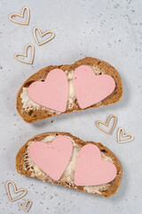 Two slices of bread with heart-shaped meat on top on a light surface seen from above during a simple meal preparation