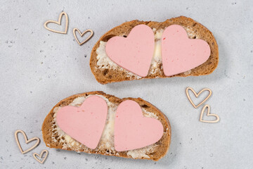 Two slices of bread with heart-shaped meat on top on a light surface seen from above during a simple meal preparation