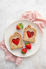 Toast with heart-shaped cutouts filled with jam and fresh strawberries on a plate with red heart decorations