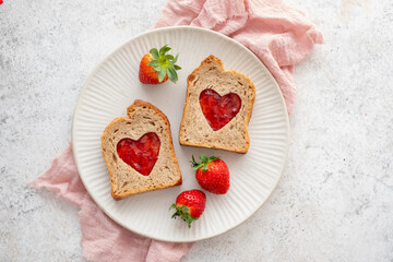 Toast with heart-shaped cutouts filled with jam and fresh strawberries on a plate with red heart decorations