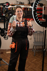 Bike mechanic in garage. Female worker blogger reviewing and recording video on smartphone waving dollar bill money winning online lottery game in bicycle workshop.