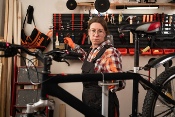 Mechanic repairing mountain bike in small workshop with tools on wall during professional service
