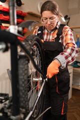 Bicycle repair in repairs workshop. Female mechanic fixing rear bicycle wheel using tools in workshop. Transport, repair, maintenance and service.