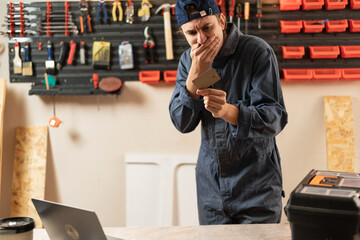 Upset worker man with credit card near laptop at working workshop