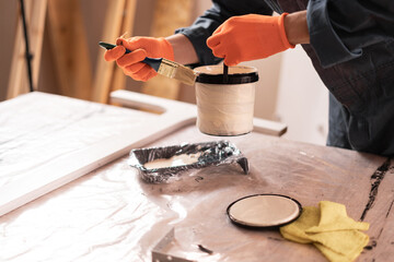 Close up of decorator hands with brush removing paint from plastic can in workshop