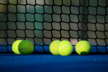Detail of tennis balls on blue synthetic turf court under sunlight.