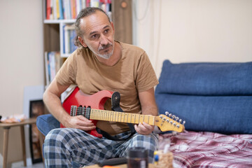 Obraz premium Man Playing Guitar at Home in His Free Time. Casual Guitar Playing at Home Lifestyle. Man Enjoying Music While Playing Guitar at Home. Home Music Session with Man Playing Guitar.