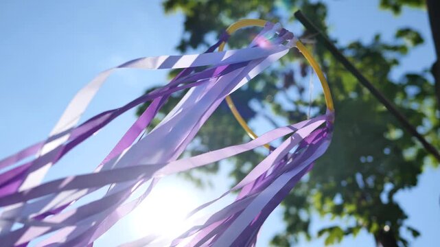Purple ribbons fluttering in wind against a sunny blue sky with green trees