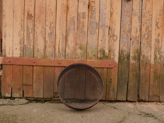 Round metal sieve leaning against old wooden doors with peeling paint.